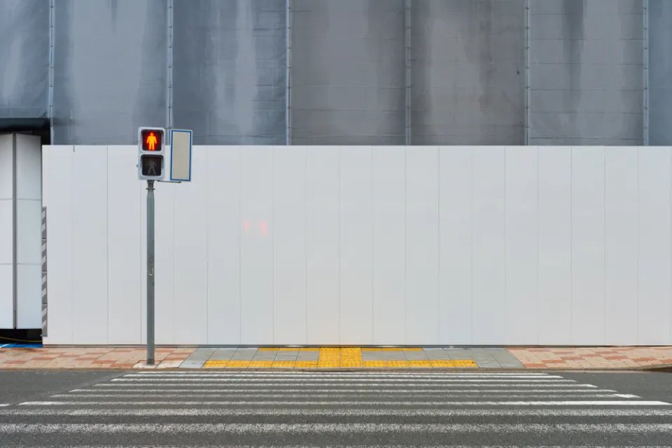 Crosswalk leading to sidewalk and blank construction wall with pedestrian crossing light